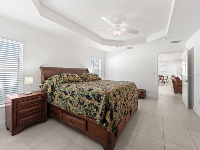 bedroom featuring ceiling fan, light tile patterned flooring, a raised ceiling, and multiple windows