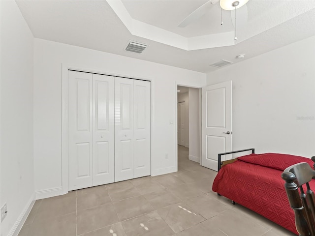 bedroom with a tray ceiling, ceiling fan, a closet, and light tile patterned flooring