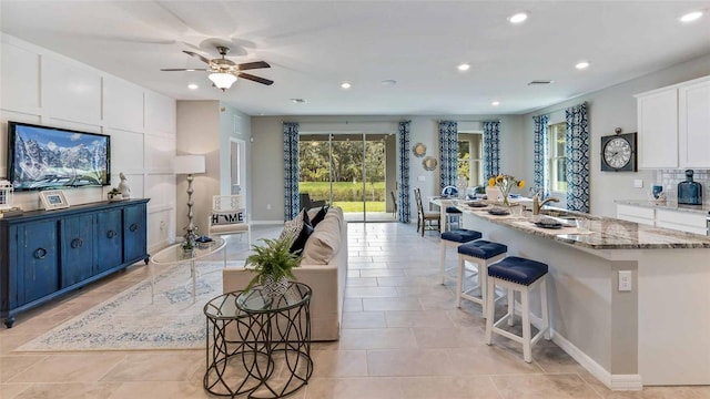 kitchen featuring ceiling fan, light stone counters, an island with sink, a breakfast bar area, and white cabinets