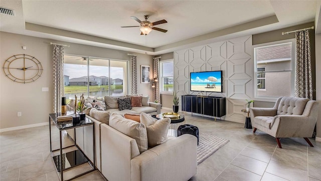 tiled living room featuring ceiling fan and a tray ceiling