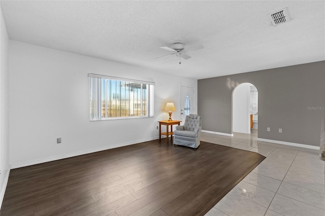 living area with a textured ceiling, light wood-type flooring, and ceiling fan