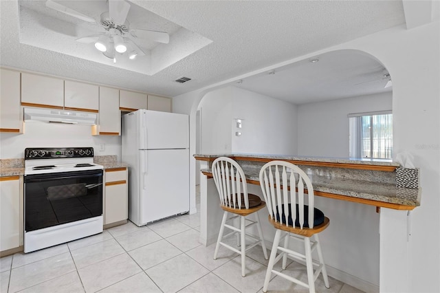 kitchen with white appliances, white cabinets, a kitchen breakfast bar, a textured ceiling, and light tile patterned flooring