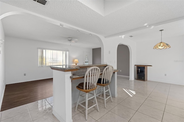 kitchen with light hardwood / wood-style floors, a kitchen bar, a textured ceiling, and hanging light fixtures