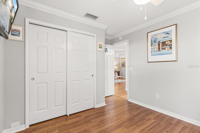 unfurnished bedroom featuring hardwood / wood-style floors, ornamental molding, and a closet