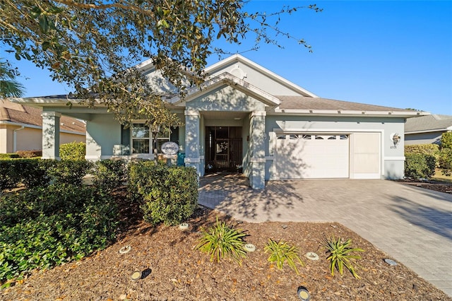 ranch-style house featuring a garage, decorative driveway, and stucco siding