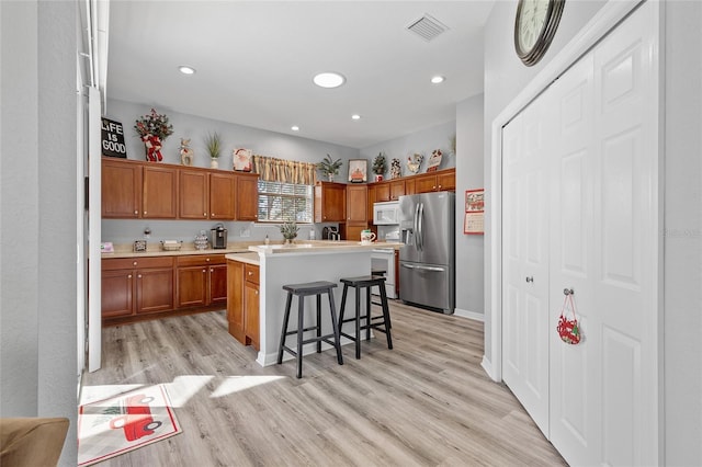 kitchen featuring a breakfast bar, light wood-type flooring, white appliances, and a center island