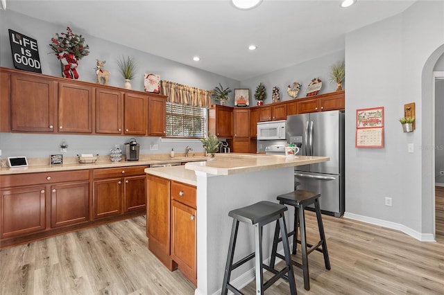 kitchen featuring sink, stainless steel fridge, light hardwood / wood-style floors, a kitchen island, and a breakfast bar area