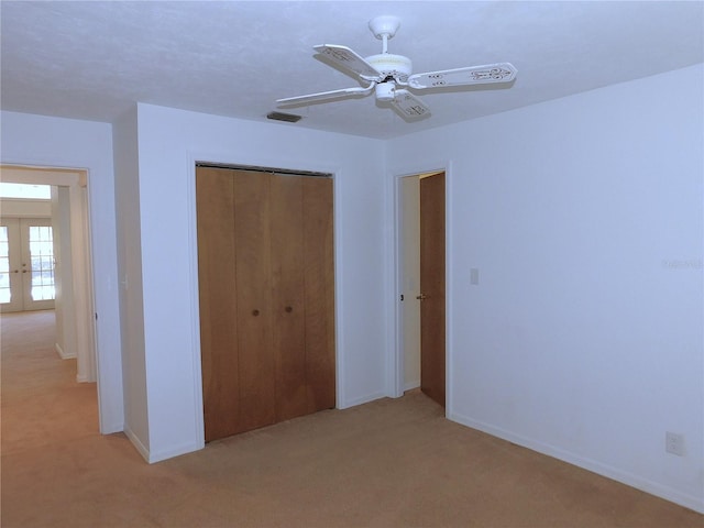 unfurnished bedroom featuring ceiling fan, french doors, light carpet, and a closet