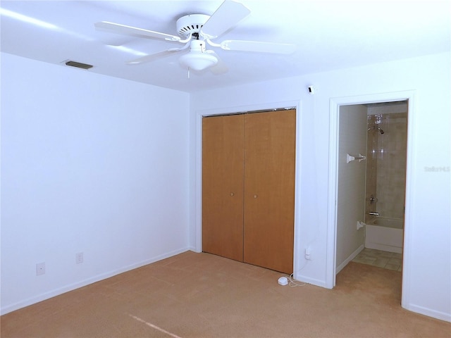 unfurnished bedroom with a closet, ensuite bath, ceiling fan, and light colored carpet