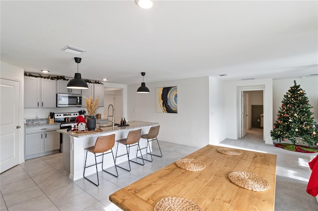 kitchen featuring a kitchen island with sink, hanging light fixtures, gray cabinets, light stone countertops, and stainless steel appliances