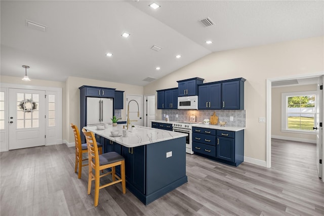 kitchen with a breakfast bar, light hardwood / wood-style flooring, vaulted ceiling, and an island with sink