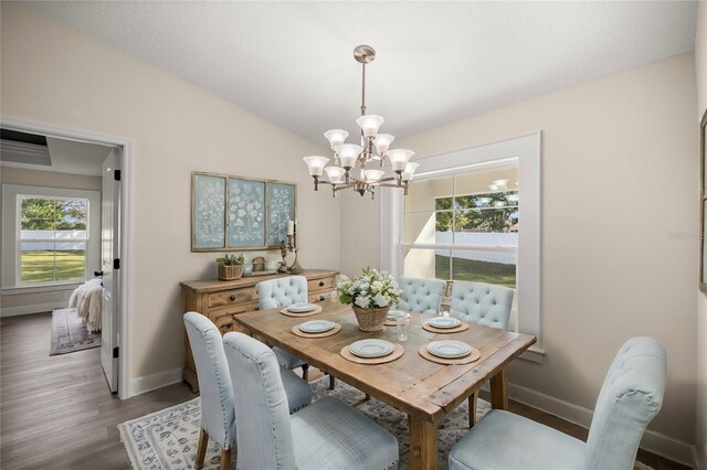 dining area with dark wood-type flooring, lofted ceiling, and a notable chandelier