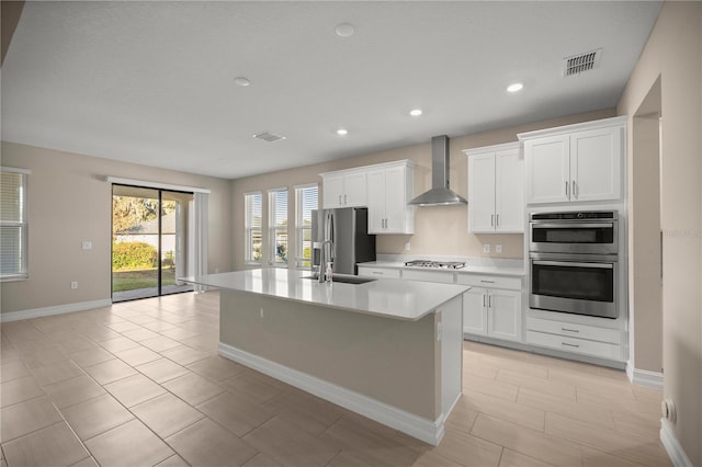 kitchen with wall chimney exhaust hood, stainless steel appliances, sink, white cabinets, and an island with sink