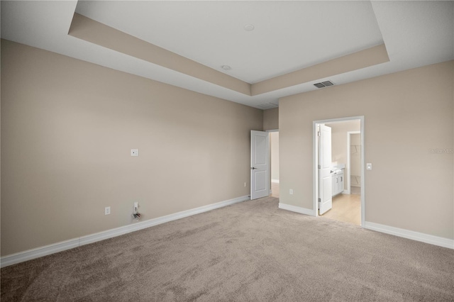 unfurnished bedroom featuring a tray ceiling, ensuite bath, and light carpet