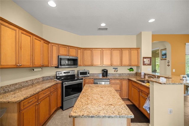 kitchen with a center island, sink, light stone countertops, kitchen peninsula, and stainless steel appliances