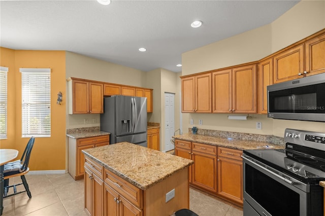 kitchen featuring light tile patterned floors, a center island, stainless steel appliances, and light stone counters