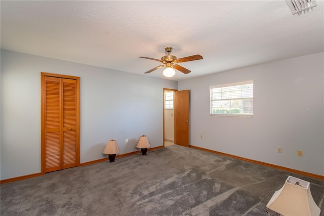 empty room with a textured ceiling, dark carpet, and ceiling fan