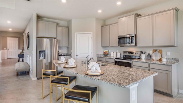 kitchen with gray cabinets, sink, stainless steel appliances, and a center island with sink