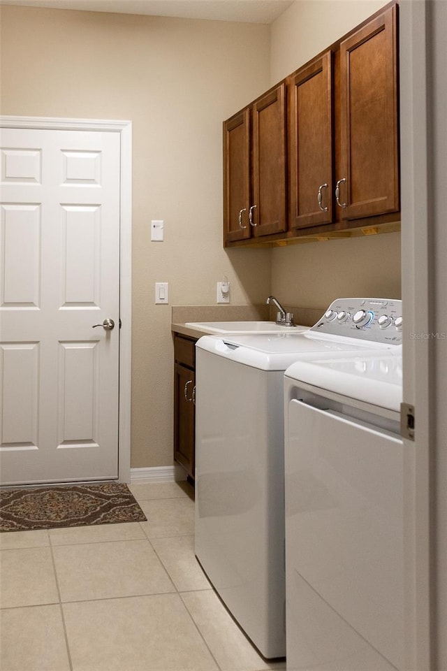 clothes washing area featuring washing machine and dryer, sink, light tile patterned flooring, and cabinets