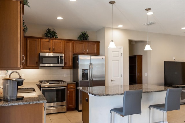 kitchen with a kitchen bar, appliances with stainless steel finishes, decorative light fixtures, dark stone countertops, and a kitchen island