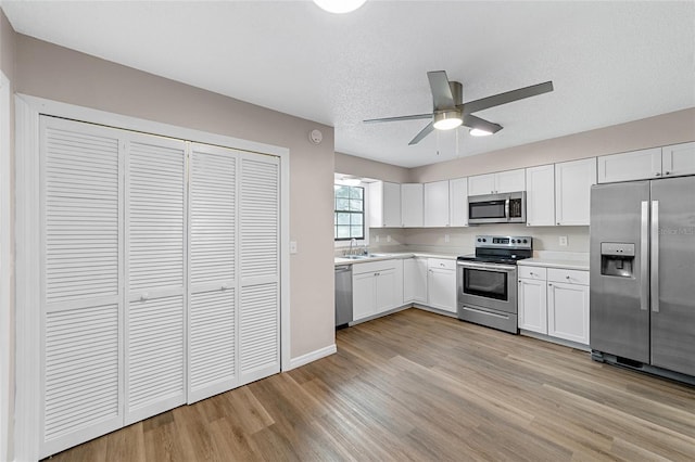 kitchen featuring white cabinets, light wood-type flooring, stainless steel appliances, and a textured ceiling