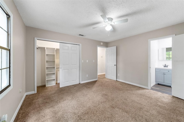 unfurnished bedroom featuring light carpet, ensuite bathroom, sink, ceiling fan, and a textured ceiling