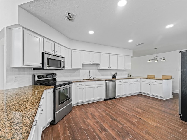 kitchen with visible vents, dark wood finished floors, a peninsula, a sink, and stainless steel appliances