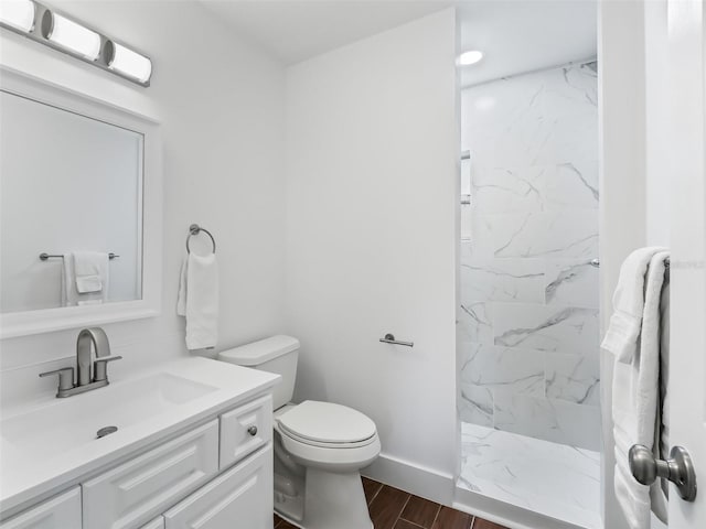 bathroom with toilet, wood finished floors, a marble finish shower, baseboards, and vanity