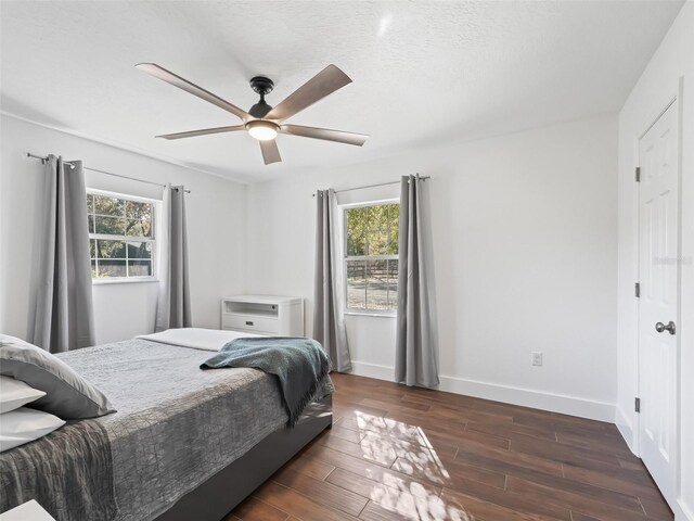 bedroom with a ceiling fan, multiple windows, dark wood-style floors, and baseboards