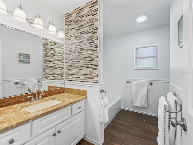 full bath featuring vanity, a bath, a wainscoted wall, and wood tiled floor
