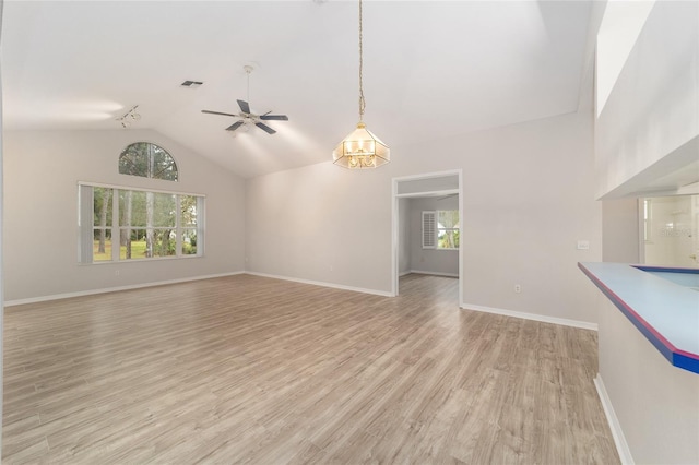 unfurnished living room featuring plenty of natural light, high vaulted ceiling, light hardwood / wood-style floors, and ceiling fan with notable chandelier