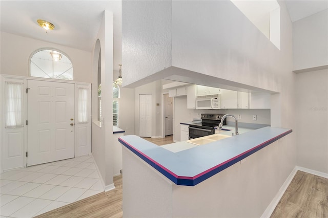 kitchen featuring kitchen peninsula, light wood-type flooring, a towering ceiling, sink, and white cabinetry