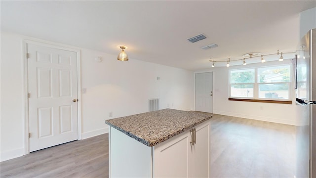 kitchen featuring white cabinets, light stone counters, stainless steel fridge, a kitchen island, and light wood-type flooring