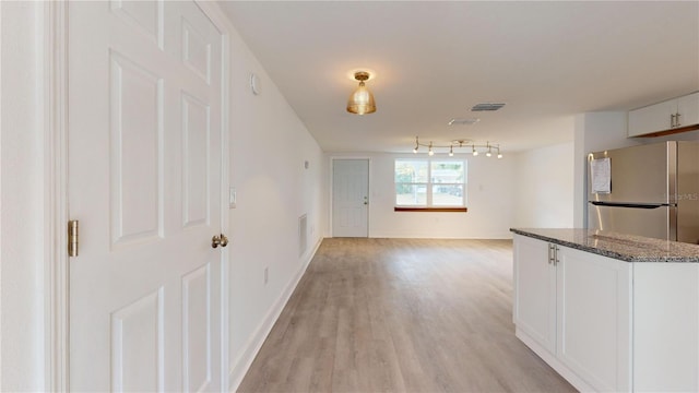 kitchen featuring light hardwood / wood-style floors, white cabinetry, stainless steel refrigerator, and dark stone counters