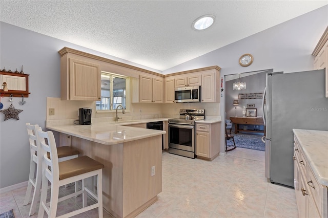 kitchen with lofted ceiling, a textured ceiling, appliances with stainless steel finishes, kitchen peninsula, and a breakfast bar area