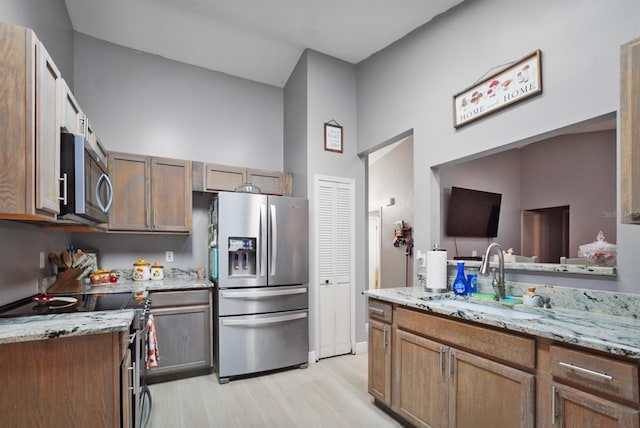 kitchen featuring light stone counters, sink, appliances with stainless steel finishes, and light hardwood / wood-style flooring