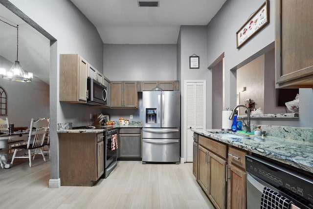 kitchen with pendant lighting, light stone counters, light wood-type flooring, and stainless steel appliances