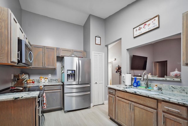kitchen featuring light wood-style flooring, light stone counters, stainless steel appliances, and a sink