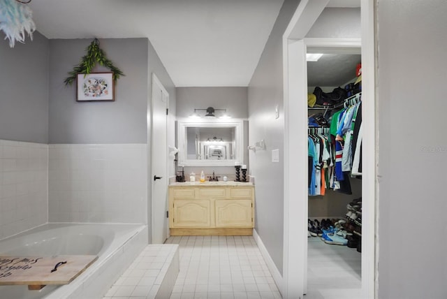 full bathroom with a walk in closet, a garden tub, vanity, tile patterned flooring, and baseboards