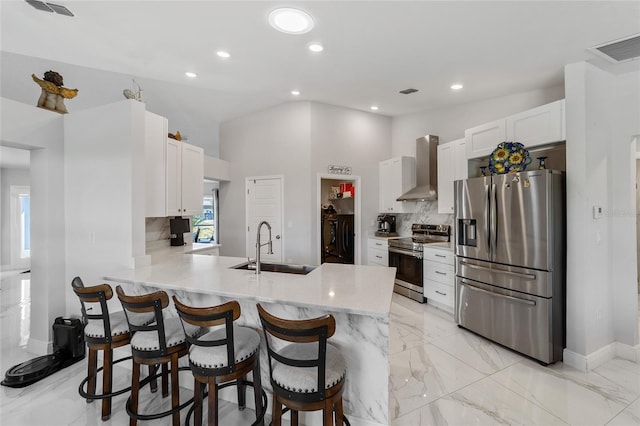 kitchen featuring kitchen peninsula, sink, wall chimney exhaust hood, appliances with stainless steel finishes, and white cabinetry