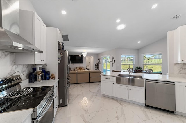 kitchen with lofted ceiling, white cabinets, wall chimney range hood, sink, and appliances with stainless steel finishes