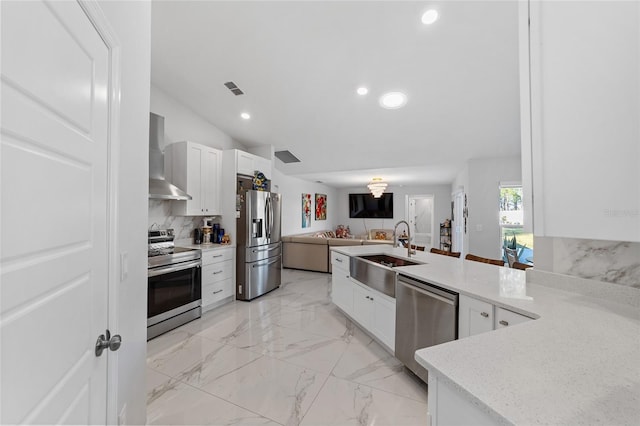 kitchen featuring lofted ceiling, wall chimney range hood, sink, appliances with stainless steel finishes, and white cabinetry