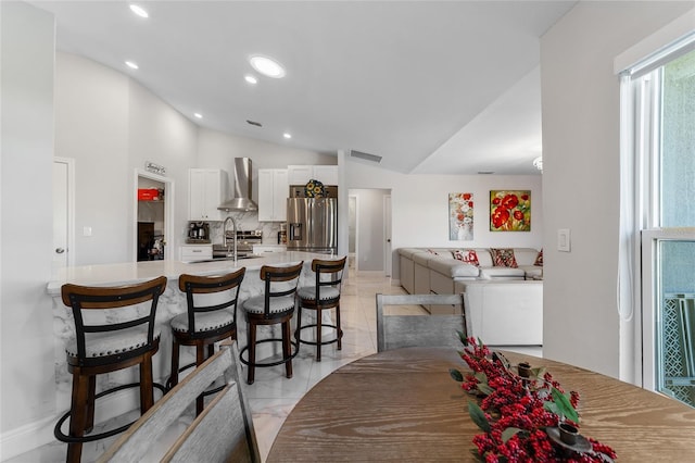 kitchen featuring sink, wall chimney exhaust hood, stainless steel refrigerator with ice dispenser, lofted ceiling, and white cabinets