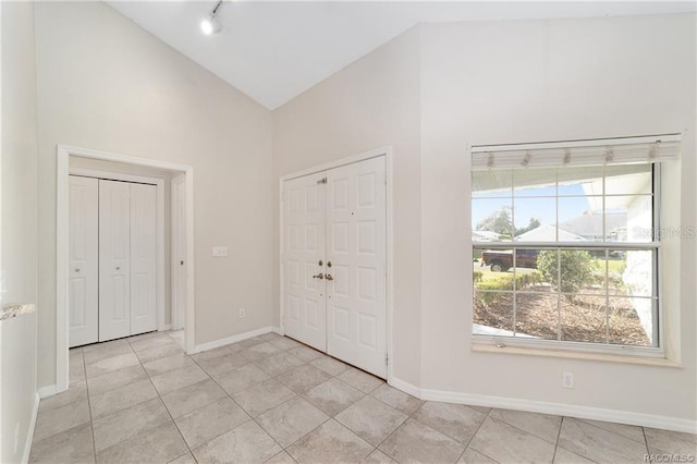 foyer entrance featuring light tile patterned floors, track lighting, and vaulted ceiling