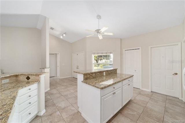 kitchen featuring white cabinetry, a center island, ceiling fan, light stone counters, and lofted ceiling