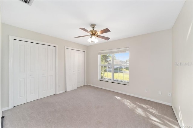 unfurnished bedroom featuring ceiling fan, light colored carpet, and multiple closets