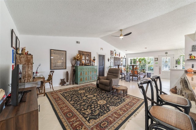 living room featuring ceiling fan, light tile patterned flooring, lofted ceiling, and a textured ceiling