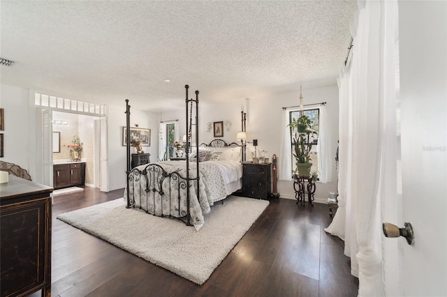 bedroom with a textured ceiling, connected bathroom, and dark hardwood / wood-style floors