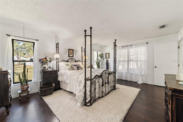 bedroom featuring multiple windows, dark wood-type flooring, and a textured ceiling