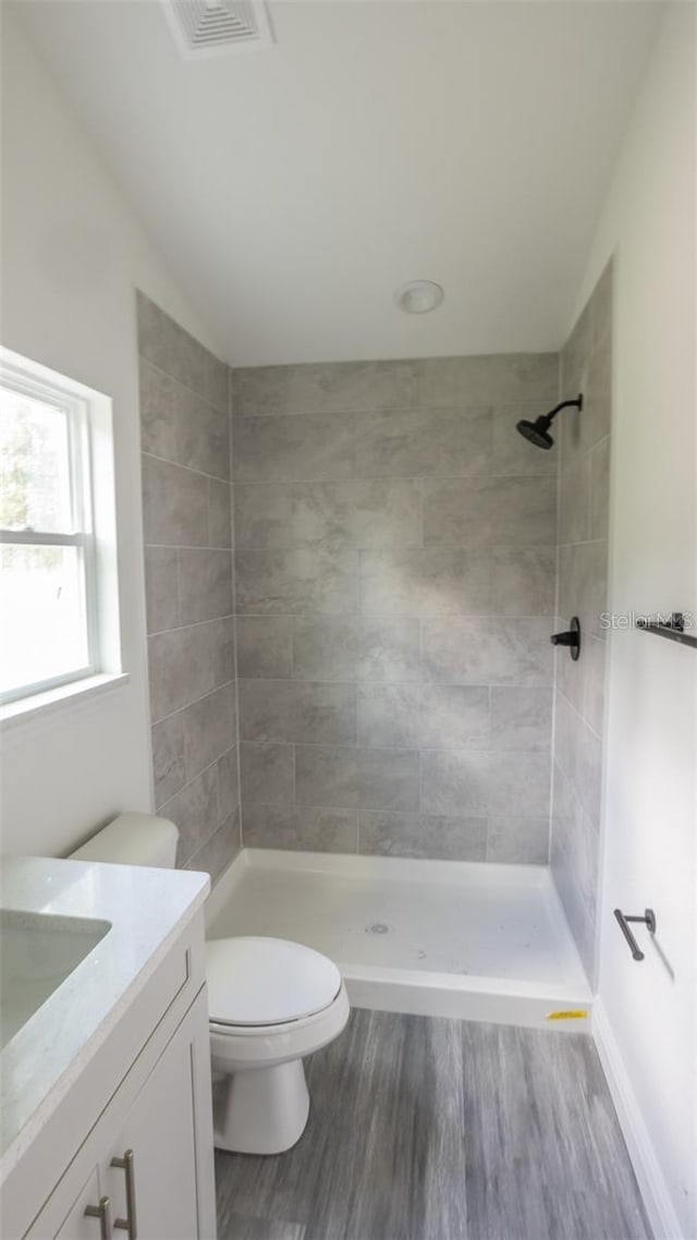 bathroom featuring tiled shower, vanity, wood-type flooring, and toilet